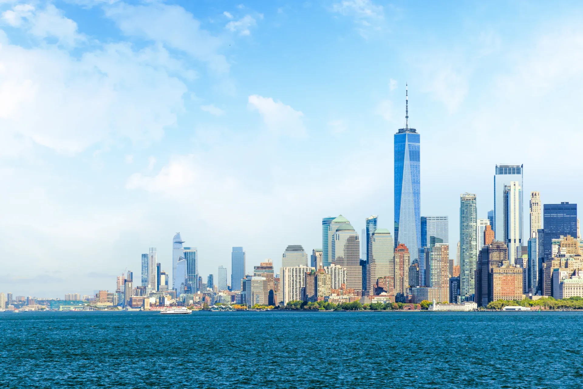 New York City skyline with Midtown and Lower Manhattan skyscrapers viewed across the water under clear daylight.