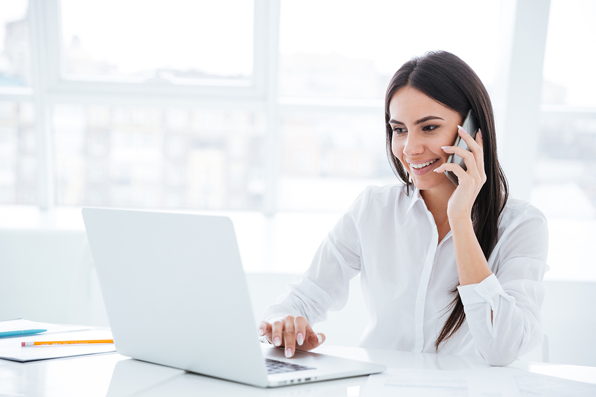 Side view of Business woman talking at phone and sitting by the table with laptop in office